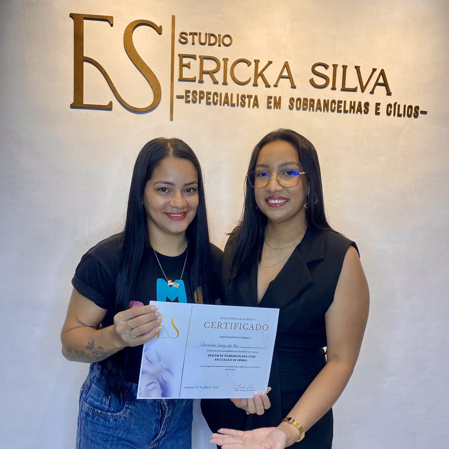 Aluna recebendo o certificado das mãos de Ericka Silva, diante do letreiro do Studio