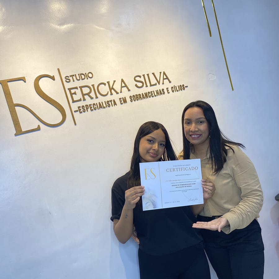 Aluna com o certificado ao lado de Ericka Silva, diante do letreiro do Studio