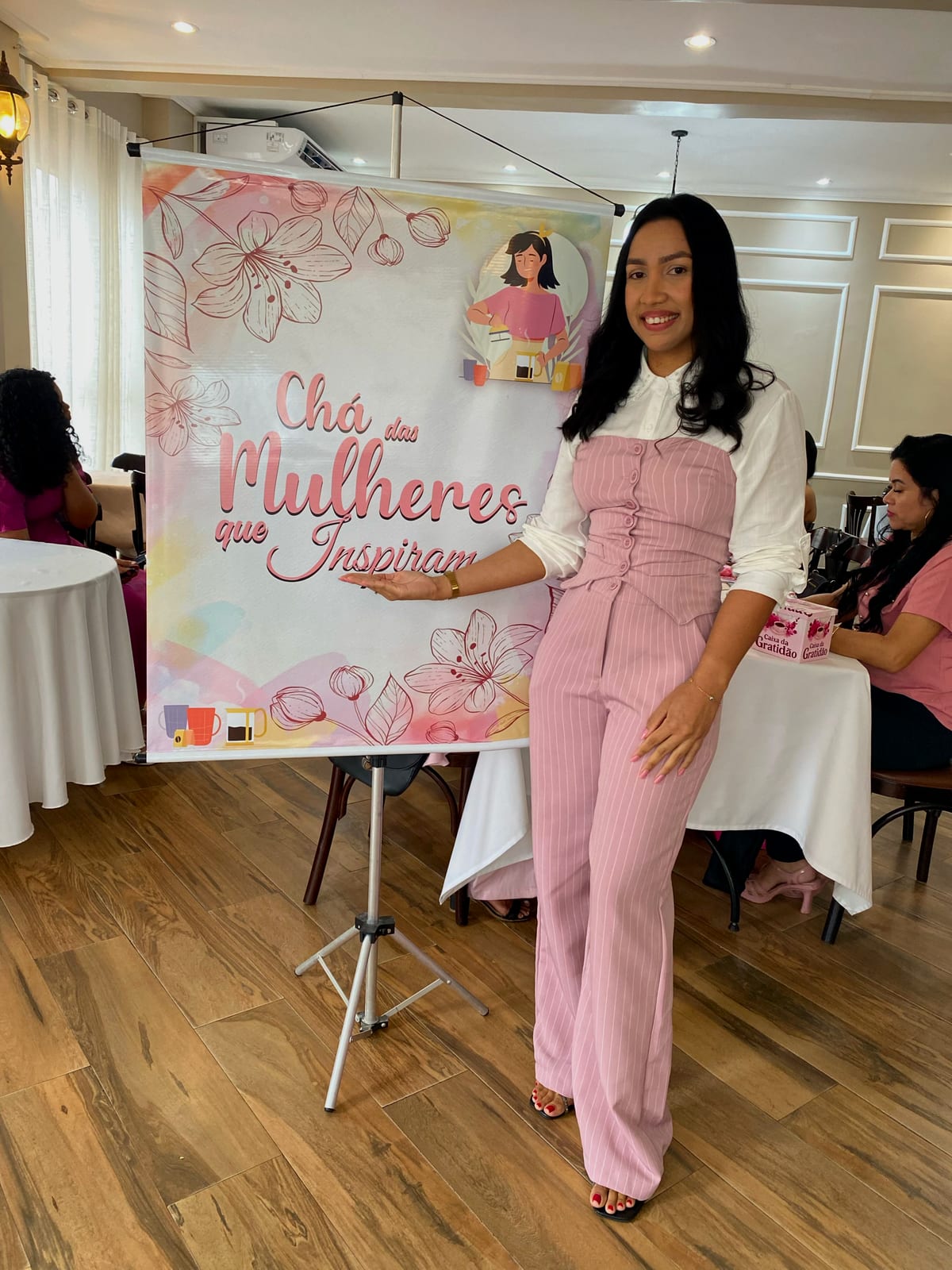 Ericka Silva ao lado do banner do Chá das Mulheres que Inspiram